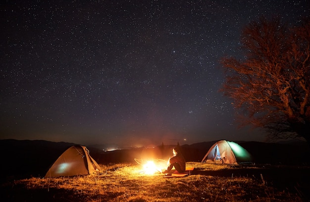 Acampamento noturno. Caminhantes descansando perto da fogueira sob o céu estrelado