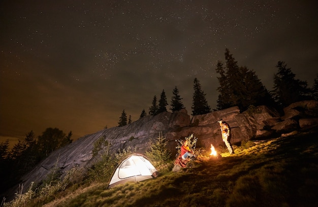 Acampamento noturno com pessoas ao redor da fogueira sob o céu estrelado