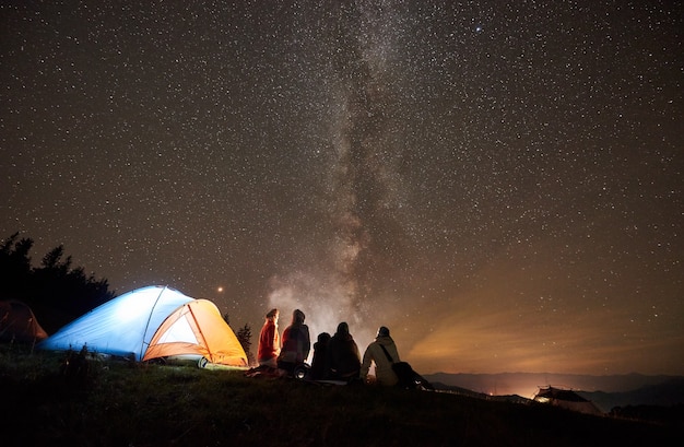 Foto acampamento noturno com pessoas ao redor da fogueira sob o céu estrelado