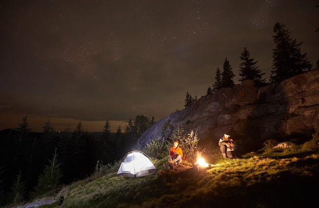 Acampamento noturno com pessoas ao redor da fogueira sob o céu estrelado