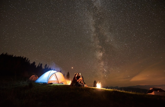 Foto acampamento noturno com pessoas ao redor da fogueira sob o céu estrelado