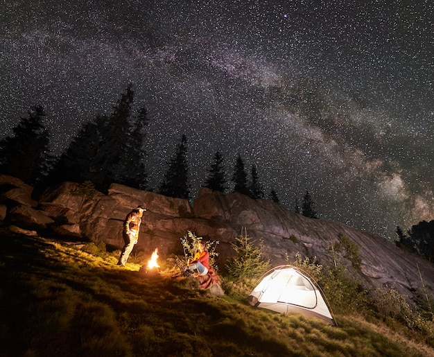Acampamento noturno com pessoas ao redor da fogueira sob o céu estrelado