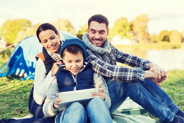 acampamento, turismo, caminhada, tecnologia e conceito de pessoas - família feliz com computador tablet pc e barraca no acampamento