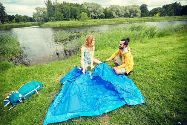 acampamento, viagens, turismo, caminhada e conceito de pessoas - casal feliz montando barraca ao ar livre