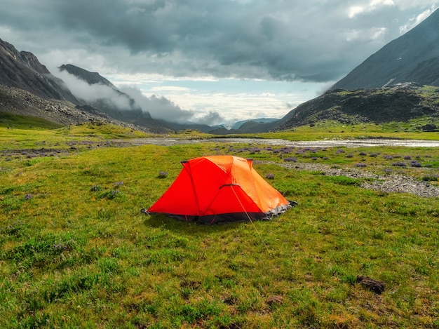 Acampar em um planalto de alta altitude verde de verão. tenda laranja depois da chuva. paz e relaxamento na natureza.