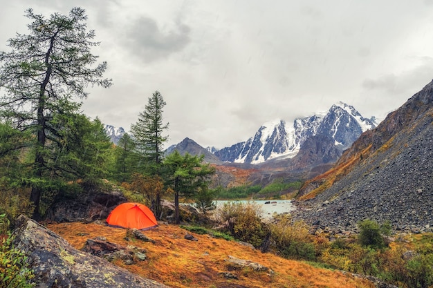 Acampar en una meseta otoñal a gran altura. Carpa naranja bajo la lluvia. Paz y relajación en la naturaleza. Lago Upper Shavlin en Altai.