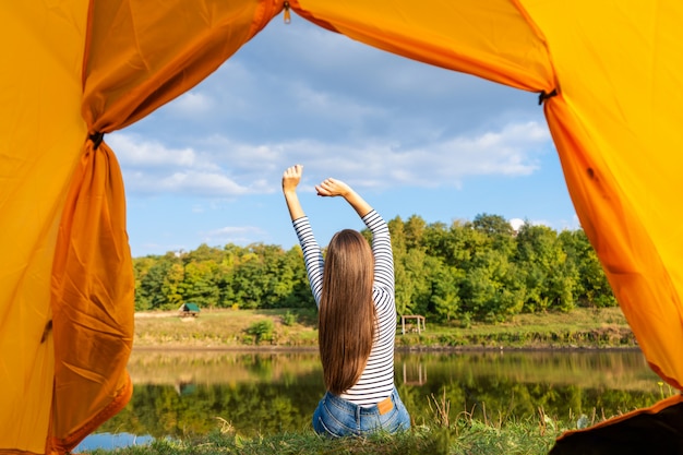 Foto acampar na margem do lago ao pôr do sol, vista de dentro da barraca do turista. a menina aprecia a natureza na frente da barraca