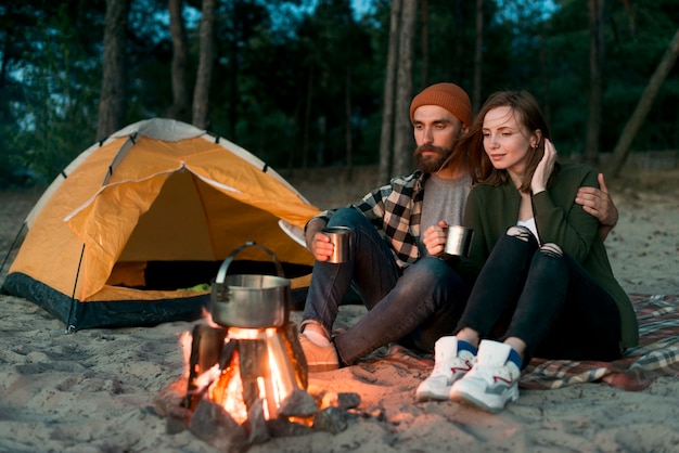 Foto acampar pareja bebiendo juntos por fogata