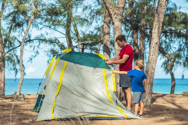 Acampar pessoas estilo de vida ao ar livre turistas montaram acampamento verde cinza floresta de verão perto do mar de lazur Menino ajuda o pai a estudar mecanismo de barraca moderna fácil de dobrar Educação natural para crianças