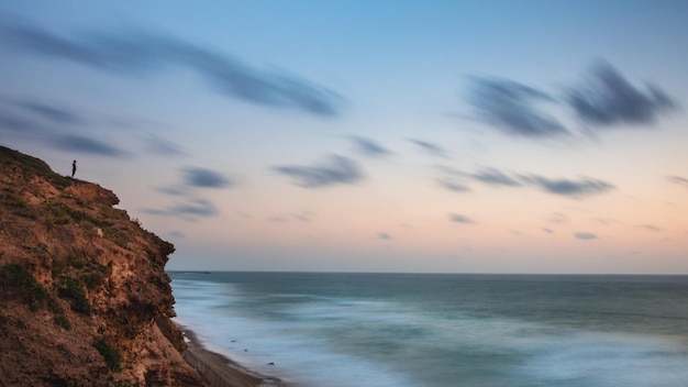 Foto un acantilado frente al mar contra el cielo durante la puesta de sol