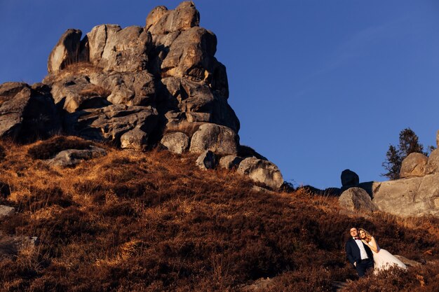 Acantilado de piedra en la cima de la montaña, los recién casados se abrazan y admiran la vista