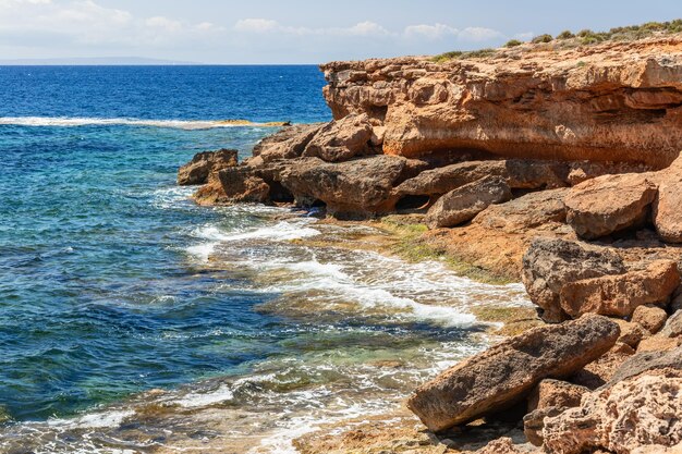 Acantilados costeros de arena kárstica de color naranja brillante borrosos por las aguas azules del mar Mediterráneo Ibiza