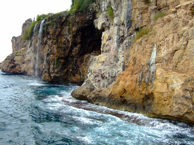 Acantilados rocosos costeros erosionados con una pequeña cascada que cae en el mar turquesa en la distancia