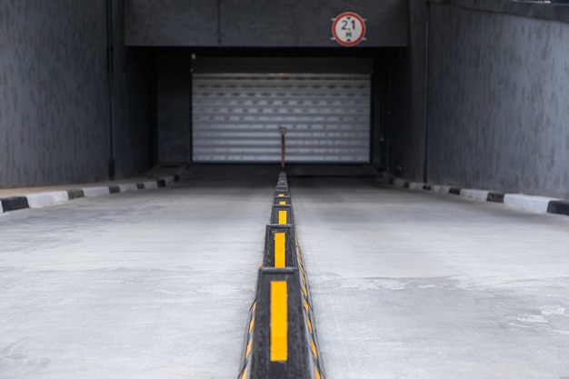 Acceso al aparcamiento subterráneo con puerta de persiana y divisores de carretera con palos amarillos.
