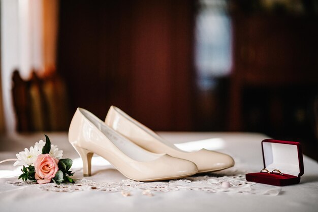 Accesorio de boda novia Elegantes zapatos beige lacados anillos de oro flores en la mesa