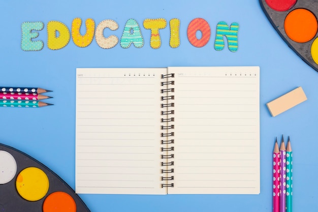 Accesorio de papelería sobre fondo azul. Útiles escolares, lápices, pinturas y libros de colores, sobre fondo azul con espacio de copia. Educación y concepto de trabajo autónomo.
