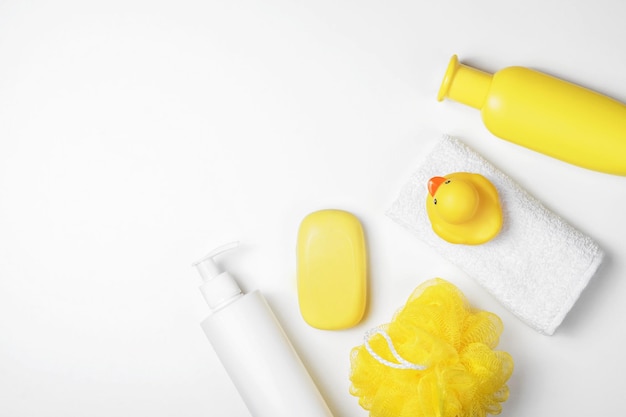 Accesorios de baño para bebés en plano. Patito de goma, champú, paño, jabón amarillo sobre un fondo blanco. Vista superior, espacio de copia