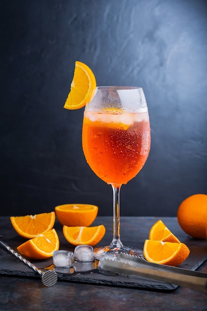 Accesorios de bar y cóctel Aperol Spritz. Cóctel italiano aperol spritz y una naranja en rodajas sobre un fondo oscuro. Aperol spritz cóctel de verano sobre una placa de pizarra