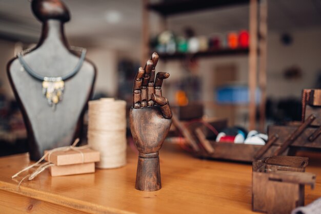 Accesorios de costura, mano de madera y maniquí con bisutería artesanal sobre la mesa en el taller, primer plano. Joyería hecha a mano