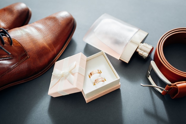 Accesorios para el día de la boda del novio. Zapatos de cuero marrón, cinturón, perfume, anillos dorados.