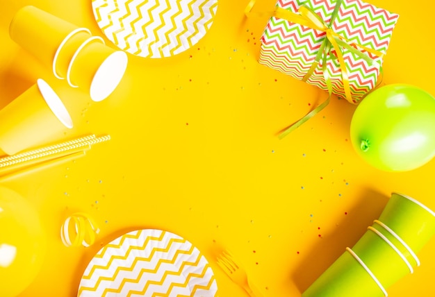 Accesorios para una fiesta o cumpleaños sobre fondo amarillo Pajitas de papel envueltas en caja de regalo tazas banderas platos Vista superior