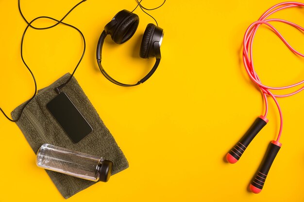 Accesorios de fitness sobre un fondo amarillo saltar la cuerda botella de toalla de agua y auriculares