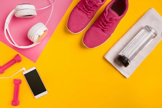 Accesorios de fitness sobre un fondo amarillo zapatillas de deporte botella de agua auriculares y pesas