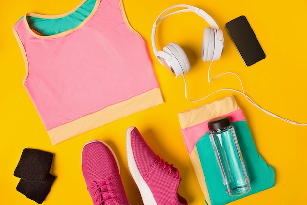 Accesorios de fitness sobre un fondo amarillo zapatillas de deporte botella de agua auriculares y top deportivo
