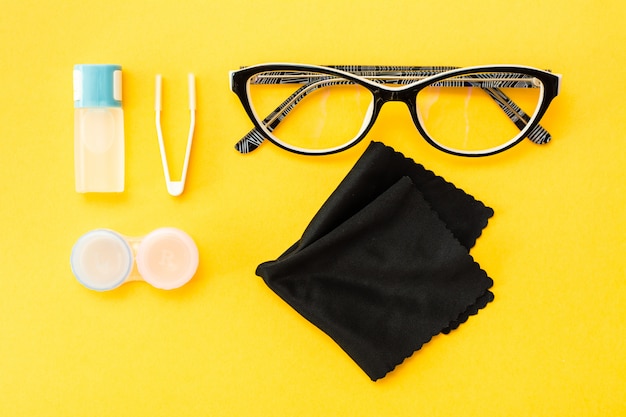 Accesorios para guardar lentes: una botella de líquido, recipiente y pinzas, gafas y tela.