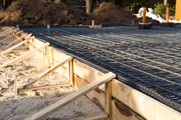 Los accesorios de hierro en un encofrado de madera con tuberías colocadas son la base para verter los cimientos de la casa con una losa de hormigón. La construcción de las villas, el diseño, las comunicaciones de ingeniería.