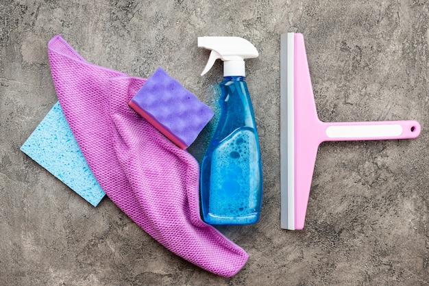 Accesorios para el hogar: spray de lavado, esponjoso, trapo y cepillos de lavado sobre un piso de yeso decorativo gris.
