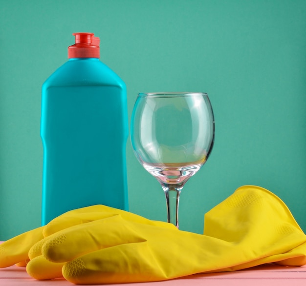 Accesorios para lavavajillas y limpieza de viviendas. Lavar platos. Botella de detergente, vidrio y guantes de goma amarilla.