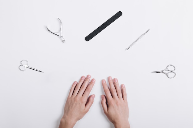 Los accesorios para la manicura se encuentran alrededor de las manos de una mujer sobre una mesa blanca.