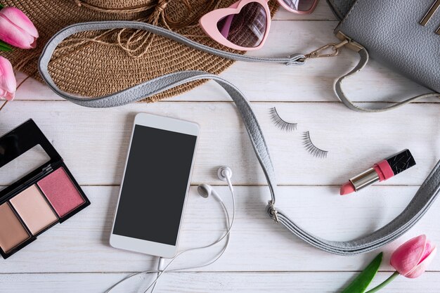 Accesorios de mujer con maquillaje, cosmética, cepillo y smartphone.