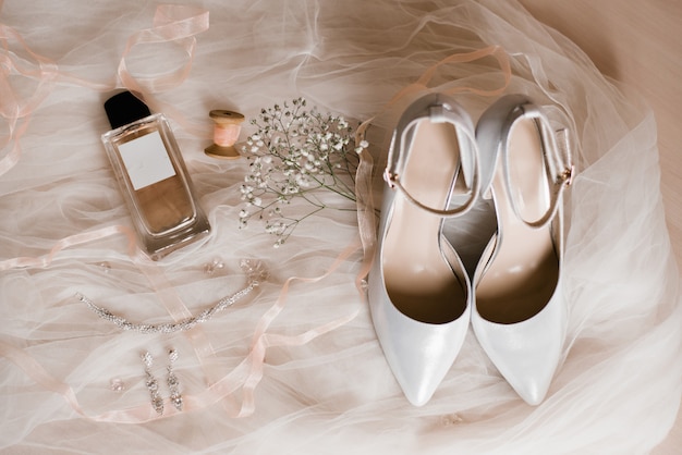 Foto accesorios de mujer: zapatos grises, agua de colonia, bisutería y una ramita de gypsophila sobre tul blanco. mañana de la novia