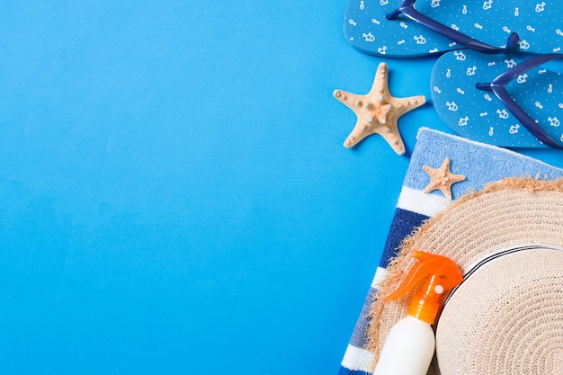 Accesorios planos de playa de verano. Crema de botella de protector solar, sombrero de paja, chanclas, toalla y conchas marinas sobre fondo de color. Concepto de vacaciones de viaje con espacio de copia.