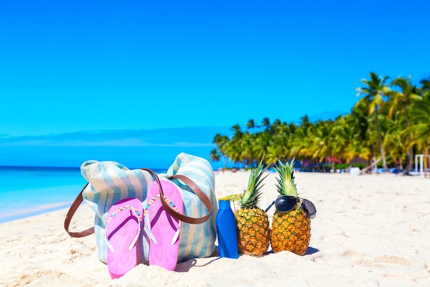 Accesorios de playa en la arena por concepto de vacaciones de verano. Bolsa, chanclas, cócteles de piña tropical piña colada y botella de loción de protección solar en la playa caribeña. Isla Saona, República Dominicana.