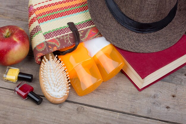 Accesorios de playa cepillo para el cabello toalla naranja sombrero crema solar loción bolsa de playa esmalte de uñas un libro sobre un fondo de madera marrón