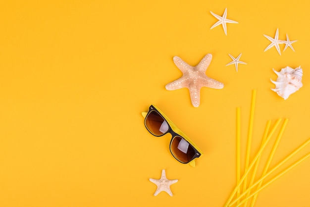 Accesorios de playa: gafas y sombrero con conchas y estrellas de mar sobre un fondo de color. Fondo de verano