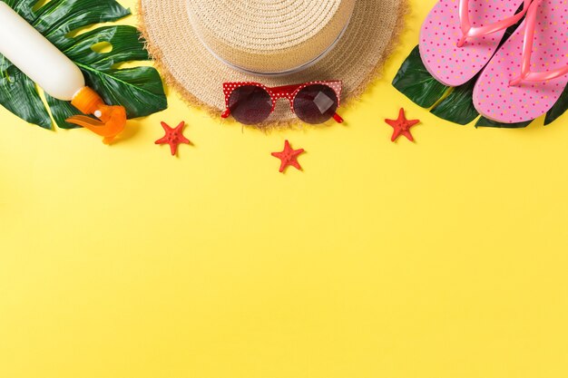 Foto accesorios de playa con sombrero de paja, botella de protector solar y estrella de mar en la vista superior de fondo amarillo con espacio de copia.