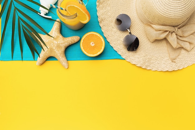 Foto accesorios de vacaciones en la playa jugo de naranja y hoja de palma sobre un fondo amarillo con una copia del espacio