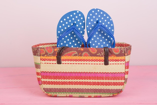 Accesorios de verano bolso de playa de paja y chanclas en mesa de madera rosa