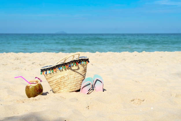 Los accesorios del verano con el coco en la playa arenosa, empañan el mar en fondo.