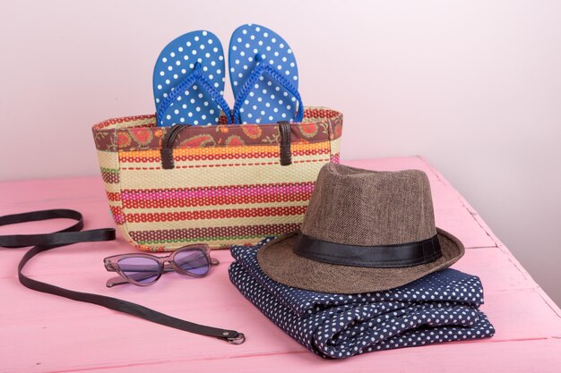 Accesorios de verano gafas de sol bolsa de playa de paja cinturón de sombrero para el sol y chanclas en la mesa de madera rosa