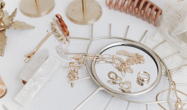 Accesorios de verano modernos Joyas doradas en pasadores de espejo boho en mesa blanca con velas