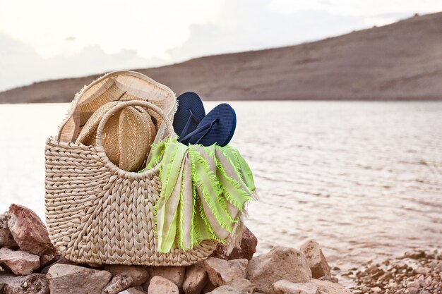 Foto accesorios de verano recogidos en una bolsa de paja en la orilla, concepto de vacaciones