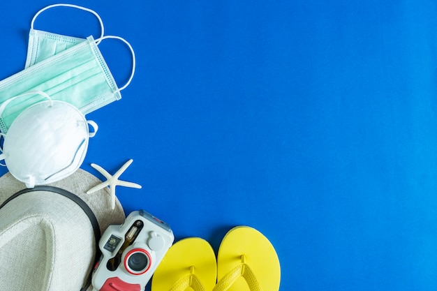 Accesorios de viaje, sombrero, cámara, zapatillas y estrellas de mar con máscara sobre fondo azul con espacio libre. Viaje de seguridad desde el concepto de virus Covid-19.