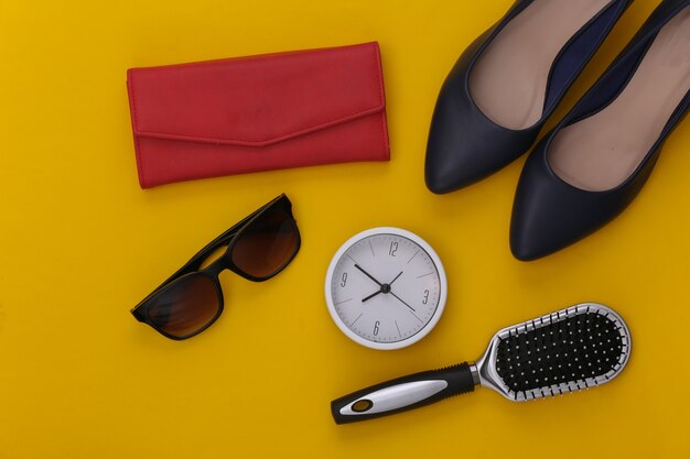 Accessoires für Damen. Schuhe mit hohen Absätzen, Geldbörse, Kamm, Sonnenbrille und Uhr auf Gelb.