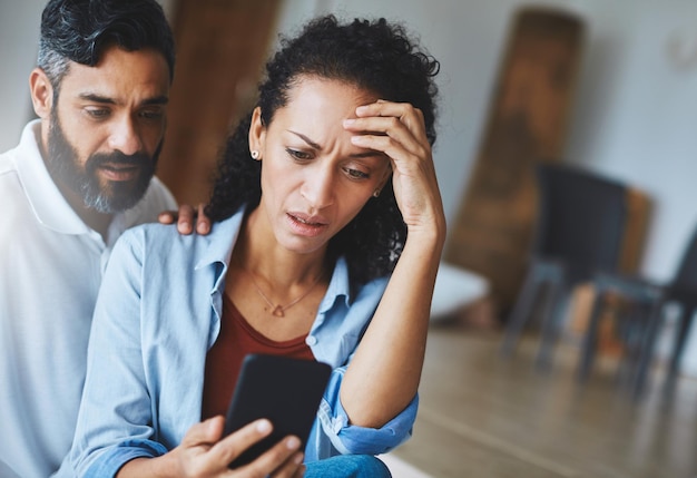 Accidentalmente le envié esa foto a tu madre. Foto de una pareja consternada que recibe malas noticias a través de un teléfono inteligente en casa.