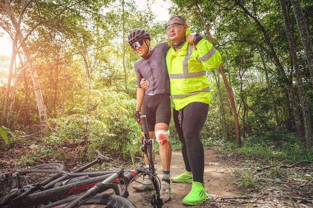 Accidente de bicicleta de montaña MTB y primeros auxilios: Choque de motociclista, lesión de rodilla y pierna, primeros auxilios para ayudar al ciclista de montaña en accidente. Equipo de primeros auxilios de atleta de bicicleta de montaña herido durante accidente de carrera.